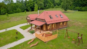 A wooden house with a red roof, a wooden deck, and a swing set. - Chalet Markoci With Hot Tub (Rakovica)