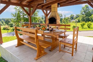 An outdoor wooden dining area with a stone oven, benches, and a view of a green landscape. - Chalet Markoci With Hot Tub (Rakovica)