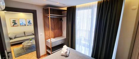 A hotel room with a bed, a seating area with a sofa and a small table, a wardrobe, and a large window with curtains.
