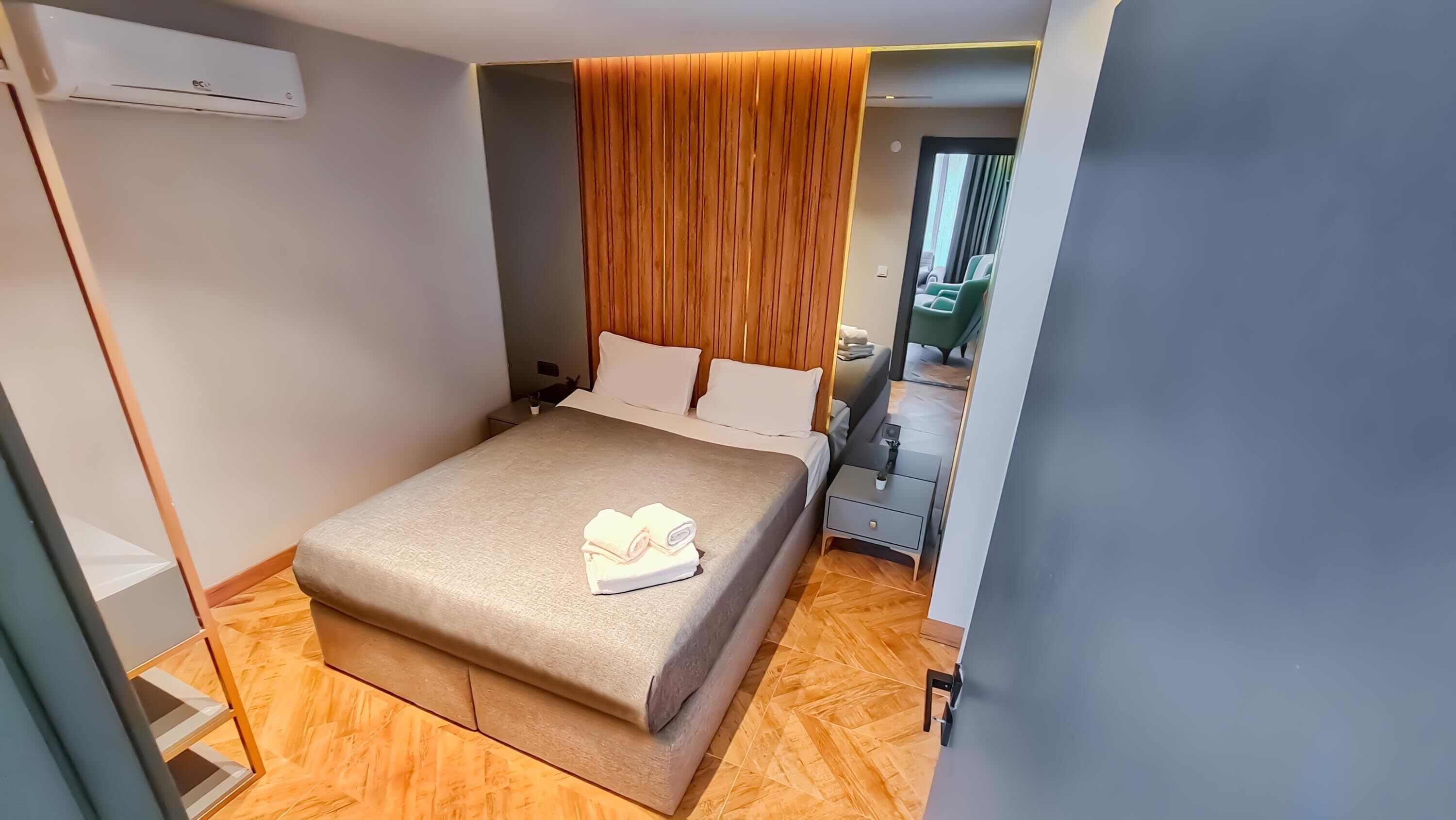 Ein modernes Hotelzimmer mit einem Bett, einem Holzkopfteil, einem kleinen Nachttisch und einem Beistelltisch.