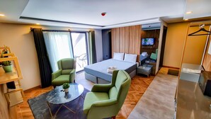 Une chambre d’hôtel moderne, équipée d’un lit, de deux fauteuils verts, d’une petite table, d’un téléviseur et d’une armoire.