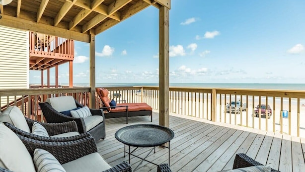 A covered outdoor deck with wicker furniture, a small round table, and a view of the ocean. - Surfside's Casa Azul - Amazing Seaside Sunrise Spot! (Surfside Beach)
