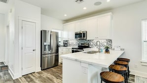 A modern kitchen with white cabinets, stainless steel appliances, a marble island, and wooden stools. - Surfside's Casa Azul - Amazing Seaside Sunrise Spot! (Surfside Beach)
