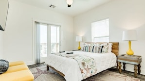 A bedroom with a bed, bedside lamps, a bench, and a view of the outdoors. - Surfside's Casa Azul - Amazing Seaside Sunrise Spot! (Surfside Beach)