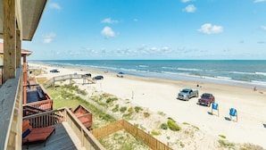 A beach view from a balcony with a wooden deck, a sandy beach, and a clear blue sky. - Surfside's Casa Azul - Amazing Seaside Sunrise Spot! (Surfside Beach)