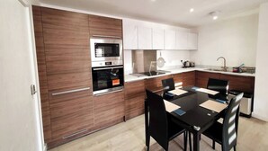 A modern kitchen with wooden cabinets, stainless steel appliances, and a dining area with a black table and chairs.