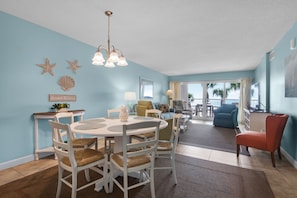 A dining area with a round table, white chairs, and a chandelier. There is a view of the balcony with palm trees. - Sandy Key 232: 2 BR / 2 BA Gulf Front Condo in Perdido Key, FL. Sleeps 6 (Pensacola)