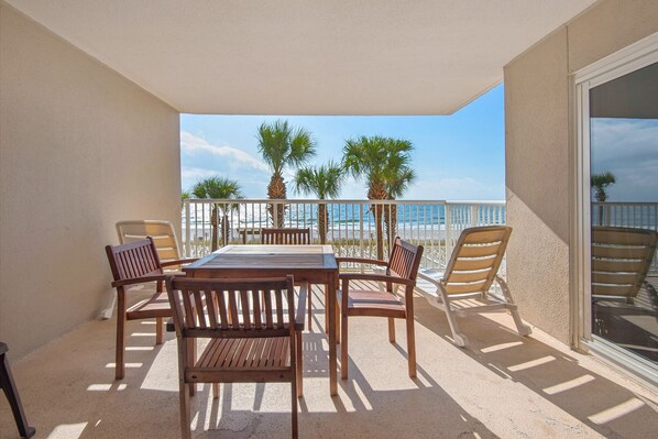 A balcony with a wooden table and chairs, overlooking a beach with palm trees and the ocean. - Sandy Key 232: 2 BR / 2 BA Gulf Front Condo in Perdido Key, FL. Sleeps 6 (Pensacola)