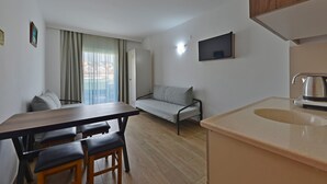 En kompakt opholdsstue med spisebord, to stole, sofa, fjernsyn og vask.