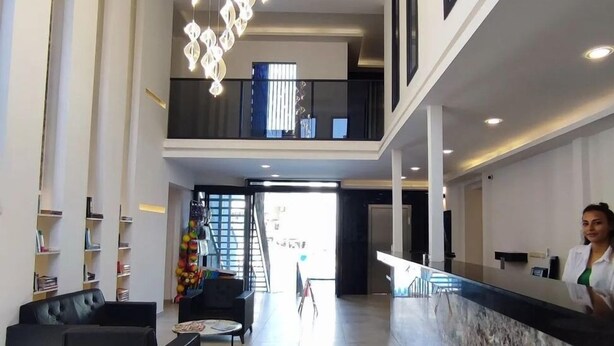 En rummelig lobby med en moderne lysekrone, en receptionsdisk og en trappe op til en etage.