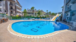 En swimmingpool med rutsjebane, omgivet af liggestole og en dæk med et gulethninglemønster.