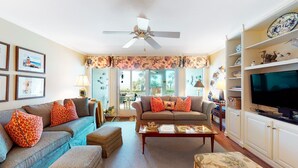 A living room with a sofa, armchair, and ottoman, a television, and a ceiling fan. - Beach Club Villa-Oceanviews in Wild Dunes- community pool & screened porch! (Isle of Palms)