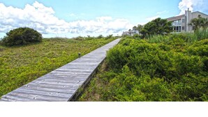 A wooden boardwalk leading to a house with a balcony, surrounded by greenery and a clear sky. - Beach Club Villa-Oceanviews in Wild Dunes- community pool & screened porch! (Isle of Palms)