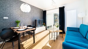 Un salon moderne avec un canapé bleu, une table à manger dressée avec des assiettes et des verres, un téléviseur et une grande fenêtre avec des rideaux.