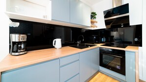 Une cuisine moderne avec des meubles de couleur bleu clair, une machine à café en acier inoxydable, une bouilloire, une hotte aspirante noire et un four encastré.