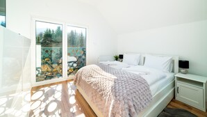 Une chambre à coucher avec un lit, une table de chevet et une vue sur les arbres, visible à travers une porte vitrée.
