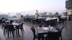 Un espace de restauration en plein air avec plusieurs tables et chaises, des guirlandes lumineuses et des plantes en pot.
