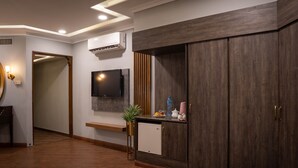 Une chambre d’hôtel moderne avec un plancher en bois, une armoire intégrée, un téléviseur à écran plat fixé au mur et un petit coin cuisine équipé d’un réfrigérateur, d’un évier et d’un plan de travail.