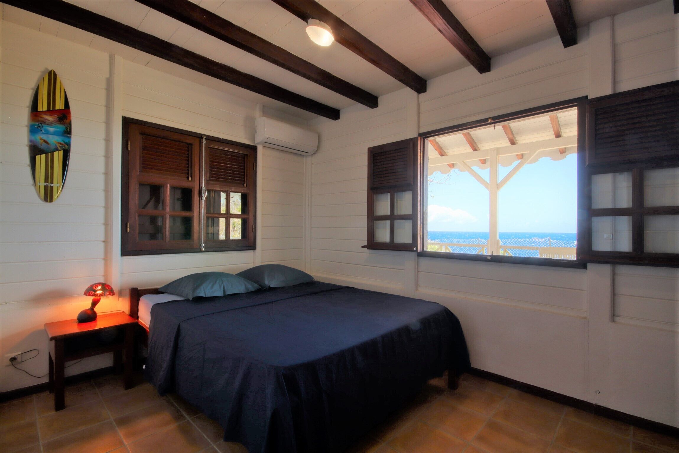 Un dormitorio con cama, mesita de noche, lámpara, decoración con una tabla de surf y ventana con vistas.