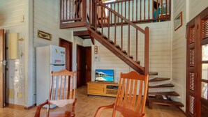 A spacious living area with a wooden staircase, a television, and two wooden chairs. - Sea-view villa with pool jacuzzi – sleeps 8 (Les Anses-d´Arlet)