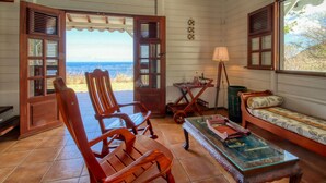 A cozy room with wooden furniture, a view of the ocean, and a table with a lamp. - Sea-view villa with pool jacuzzi – sleeps 8 (Les Anses-d´Arlet)