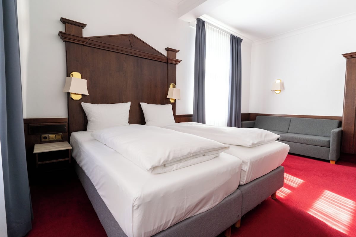 A hotel room with a large bed, two bedside tables, a sofa, and a window with curtains.