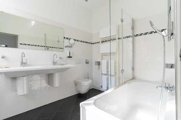 A modern bathroom with a large white bathtub, a sink with two faucets, a toilet, and a glass-enclosed shower area.