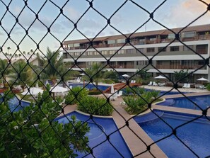 A hotel with multiple swimming pools, a covered area with lounge chairs, and a building with balconies. - Malawi Slin Resort Muro Alto (Ipojuca)