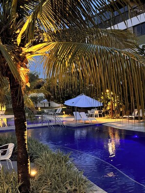 A swimming pool with lounge chairs and umbrellas, surrounded by palm trees and a building in the background. - Malawi Slin Resort Muro Alto (Ipojuca)