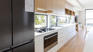 A modern kitchen with a stainless steel refrigerator, white cabinetry, and a built-in oven. - Ohana on Hungerford (kingscliff)