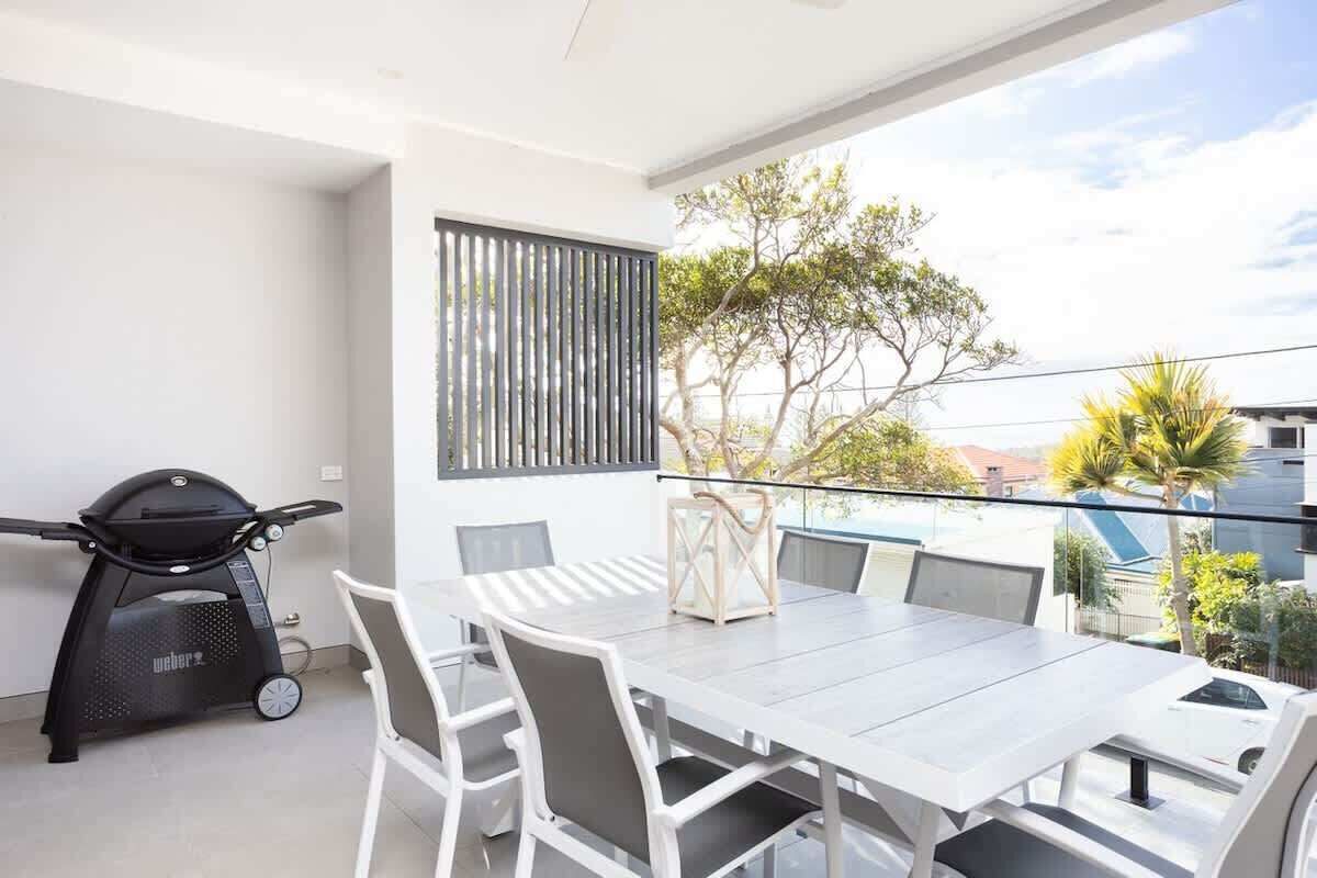 Un balcon avec une table et des chaises pour prendre les repas, un barbecue et une vue sur les arbres et les bâtiments.
