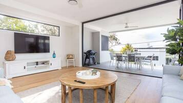 A modern living room with a flat-screen TV, a round wooden coffee table, and a large sliding glass door leading to an outdoor patio.