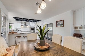 Une cuisine moderne avec des meubles blancs, un îlot central et un coin repas comprenant une table et des chaises en bois.