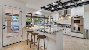 A modern kitchen with a large island, white cabinetry, stainless steel appliances, and a view through a glass door. - Amazing- Pool Home- Fire Pit & Ping Pong Table (Mesa)