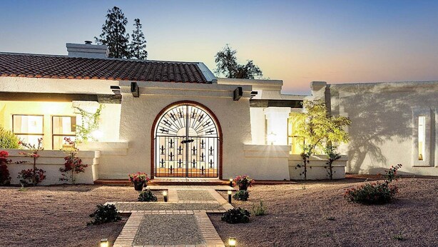 A building with a large arched entrance, a tiled roof, and a gravel driveway. - Amazing- Pool Home- Fire Pit & Ping Pong Table (Mesa)