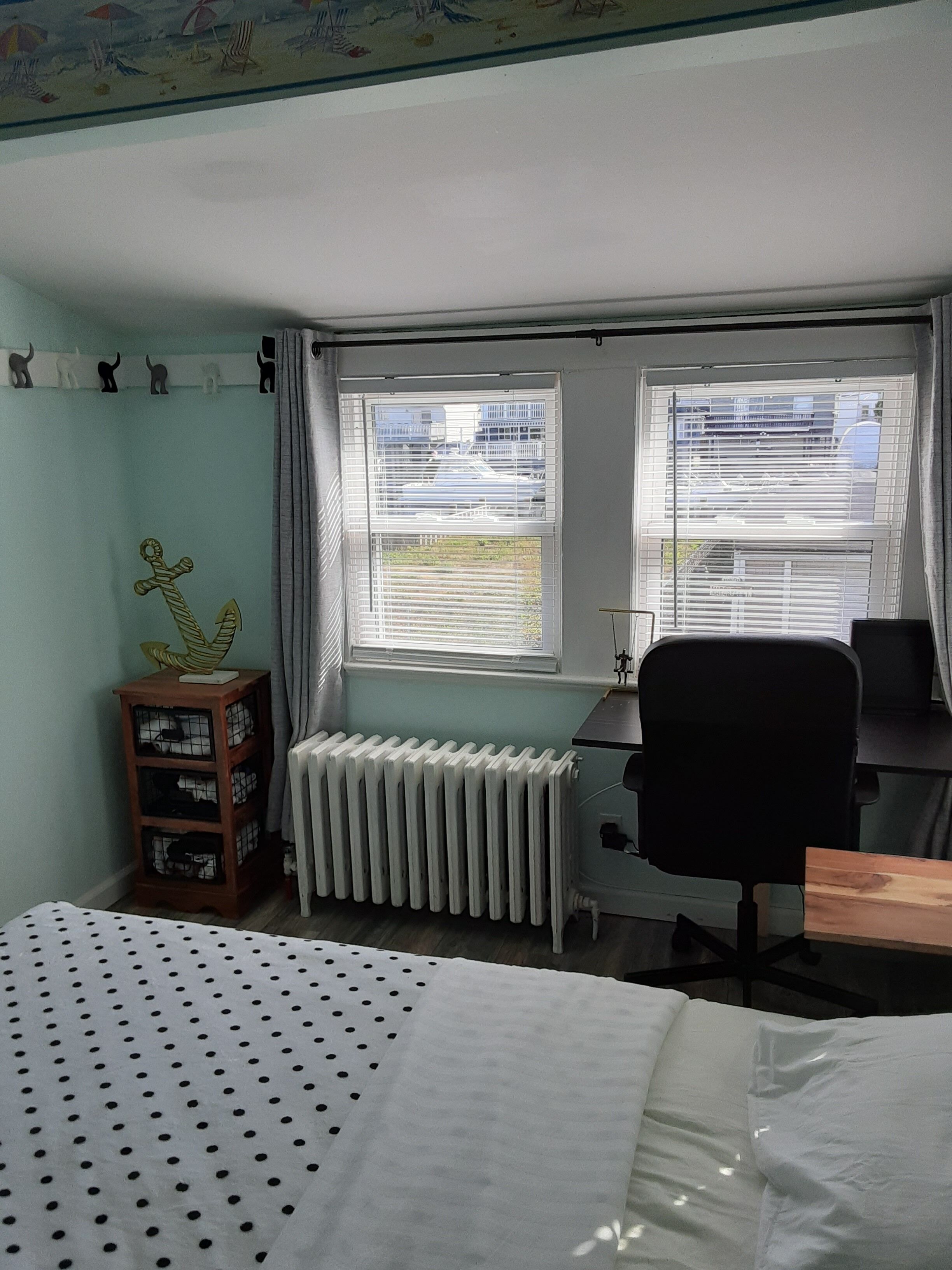 Una camera da letto con un letto, una scrivania, una sedia, un termosifone e uno scaffale con oggetti decorativi.