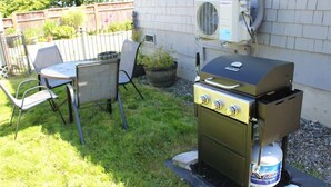 An outdoor grill area with a gas tank, a table, and chairs.