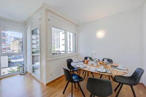 A modern dining area with a wooden table, black chairs, and a view of the street through large windows. - Locarno Place (Locarno)