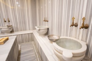 A bathroom with a marble wall, a large bathtub, two sinks, and a bidet. -  Orange Hotel & Spa (Istanbul)