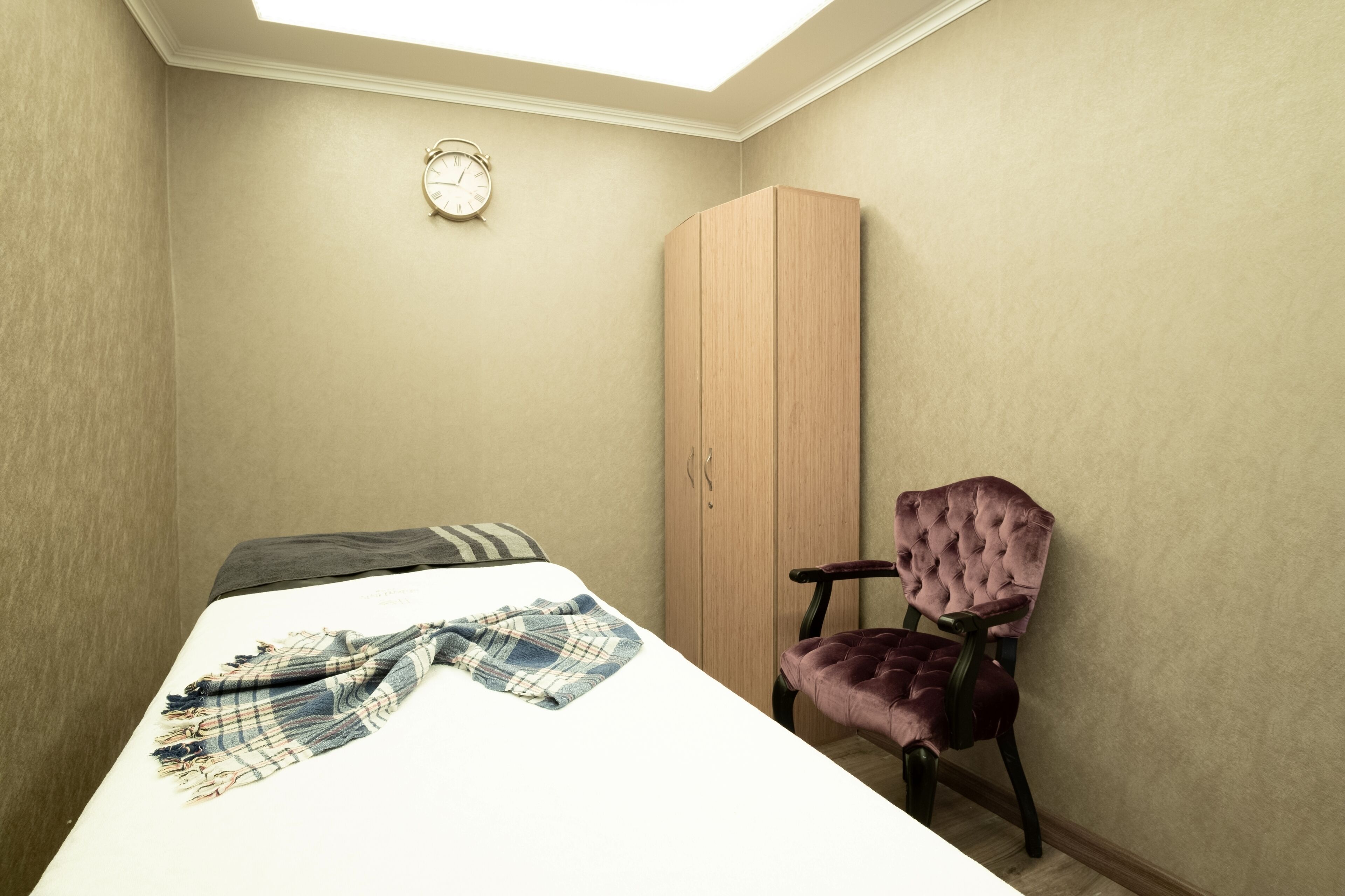 A bedroom with a bed, a wardrobe, a chair, and a clock on the wall.