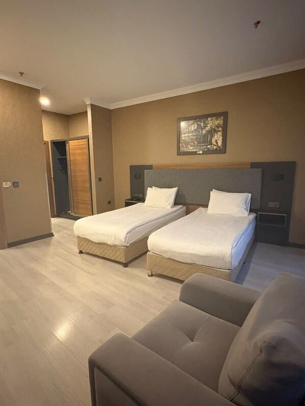 Una habitación de hotel con dos camas, un sofá, un cuadro en la pared y una puerta de madera.