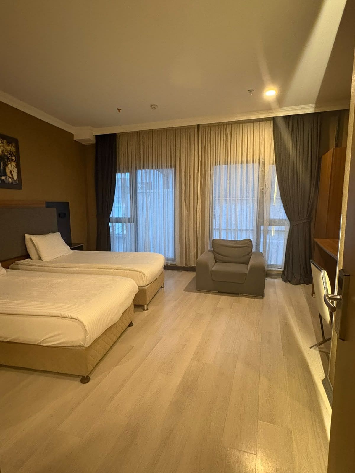Habitación de hotel con dos camas, un sofá, un televisor y ventanas amplias con cortinas.