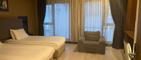 Habitación de hotel con dos camas, un sofá, un televisor y ventanas amplias con cortinas.