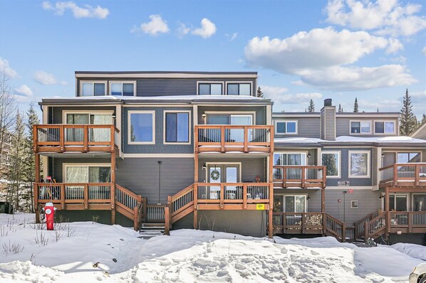 A multi-story residential building with balconies, a central staircase, and a snow-covered ground.