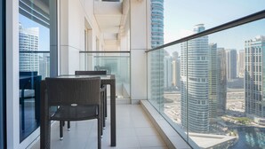 A modern balcony with a glass railing, wicker furniture, and a city view. - Maison Privee - Premium Apartment in the Heart of JLT (Dubai)