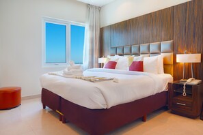Une chambre d’hôtel moderne avec un grand lit, une tête de lit en bois, une table de chevet avec une lampe et une fenêtre avec des rideaux.