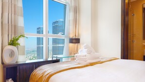 A hotel room with a large bed, a window with a city view, a bedside table with a lamp, and a bathroom door. - Maison Privee - Premium Apartment in the Heart of JLT (Dubai)