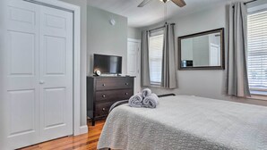 Un dormitorio con una cama, un tocador, un televisor y un ventilador de techo.