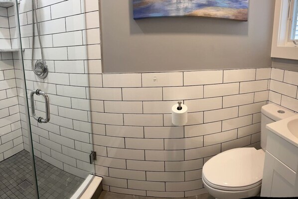 Un baño con azulejos blancos tipo metro, una cabina de ducha de cristal, un inodoro y un cuadro en la pared.