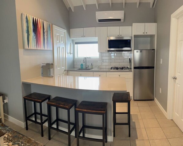 A modern kitchen with white cabinets, a stainless steel refrigerator, a microwave, and a large island with bar stools. - Prime Location, Steps to Beach 2 BR 1 BA w/Parking (Point Pleasant Beach)